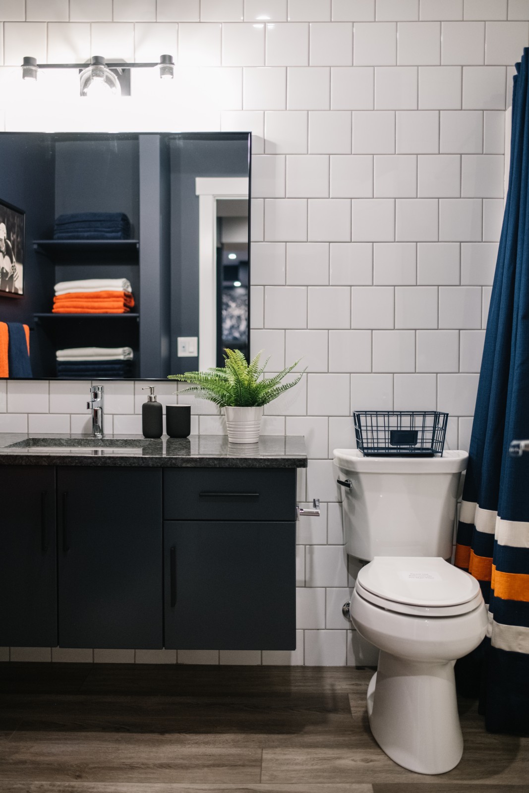 Oilers Fan Cave bathroom with dark blue vanity and dark countertops and white tile from floor to ceiling behind the toilet