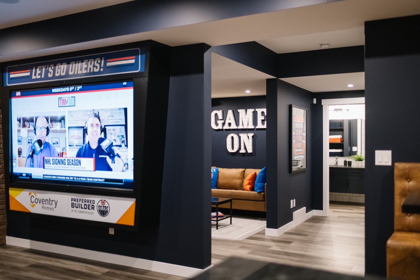 Oilers Fan Cave with large wall mounted jumbotron at front of photo, looking in to another room with the words 