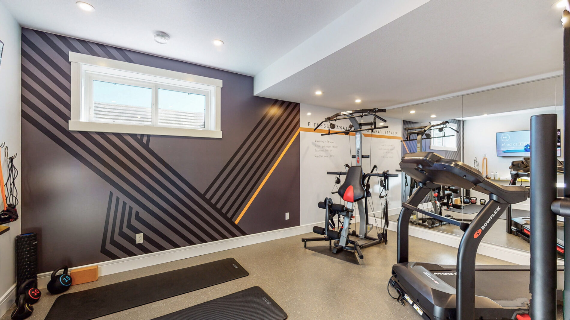 Home gym in Kail showhome with custom wall detail on wall including a white board, light rubber floor, floor to ceiling mirrors on one wall and gym equipment centered in room