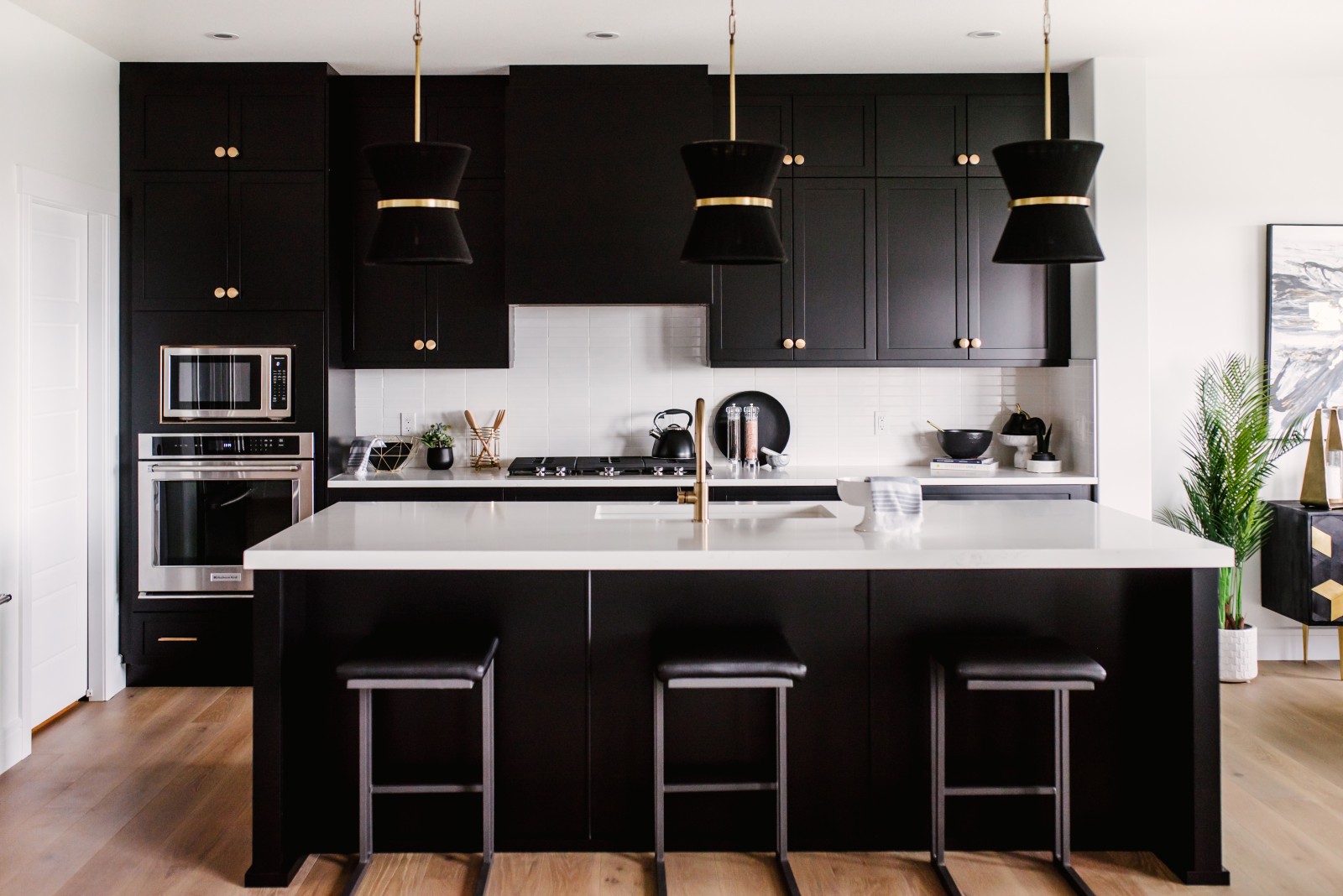 Stunning kitchen with black cabinets, white countertops and backsplash tile and gold accents in light fixtures, faucet and cabinet handles