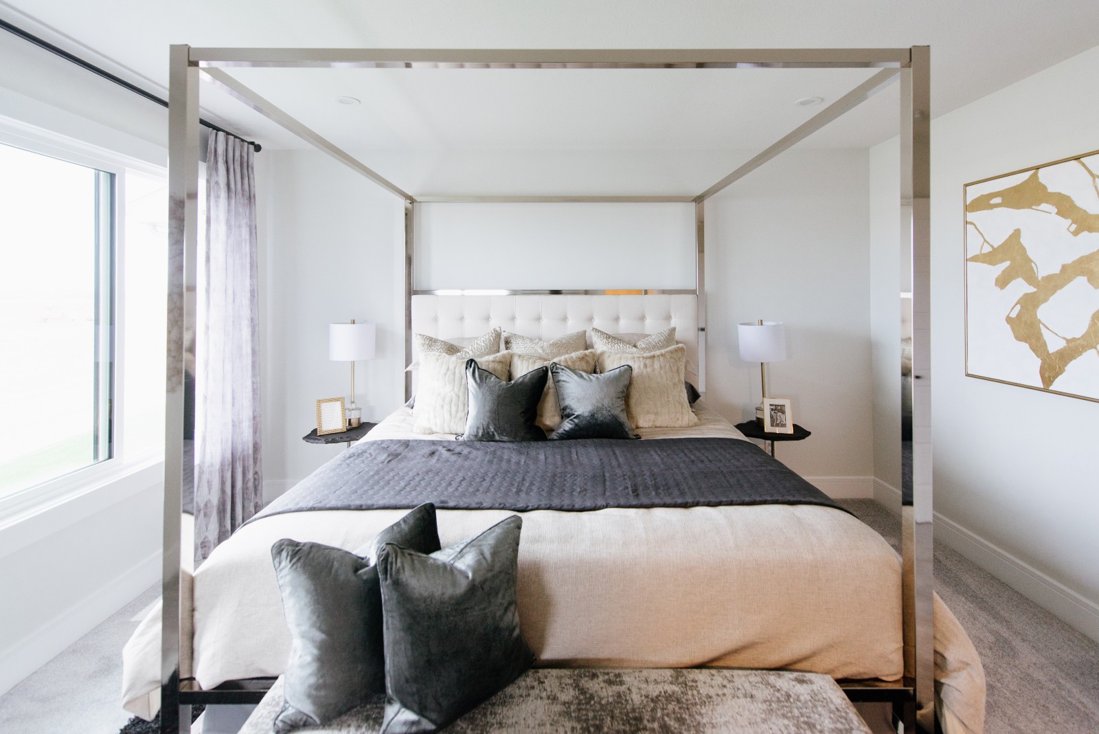 Modern master bedroom featuring sleek, chrome canopy bed, and luxurious grey and beige bed linens and pillows