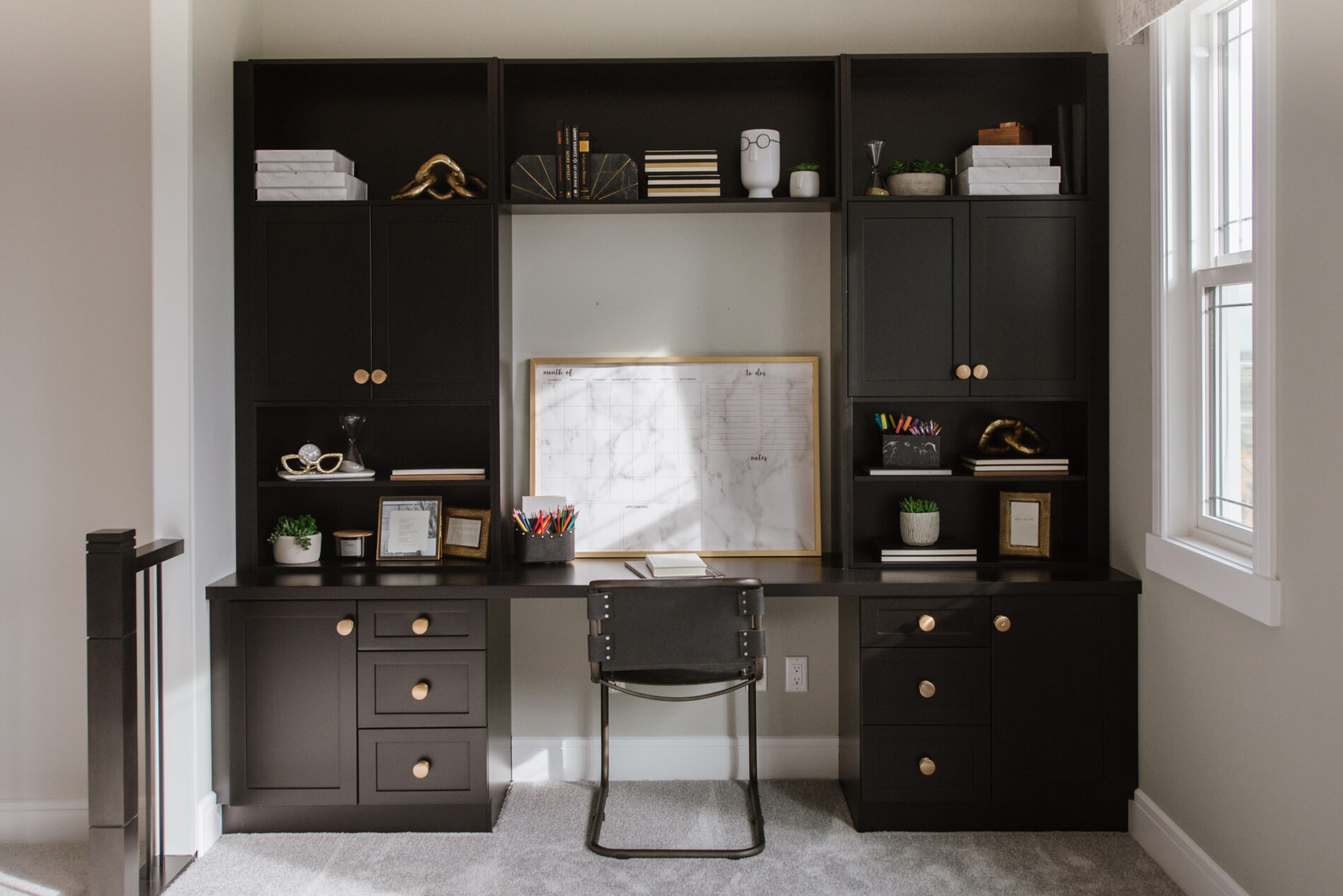 Built in study desk in luxurious black cabinets with large gold cabinet handles, and lots of space to display accessories