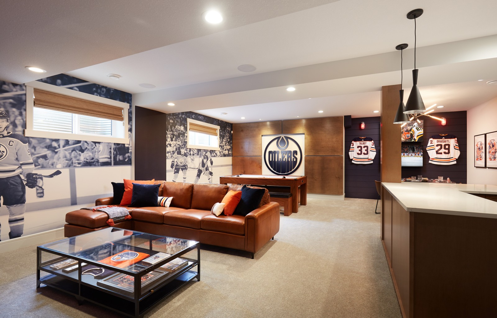 Full room photo of Oilers Fan Cave in Archer Showhome that features warm woods, large mural that spans the far wall, cozy brown leather couch and blue accents