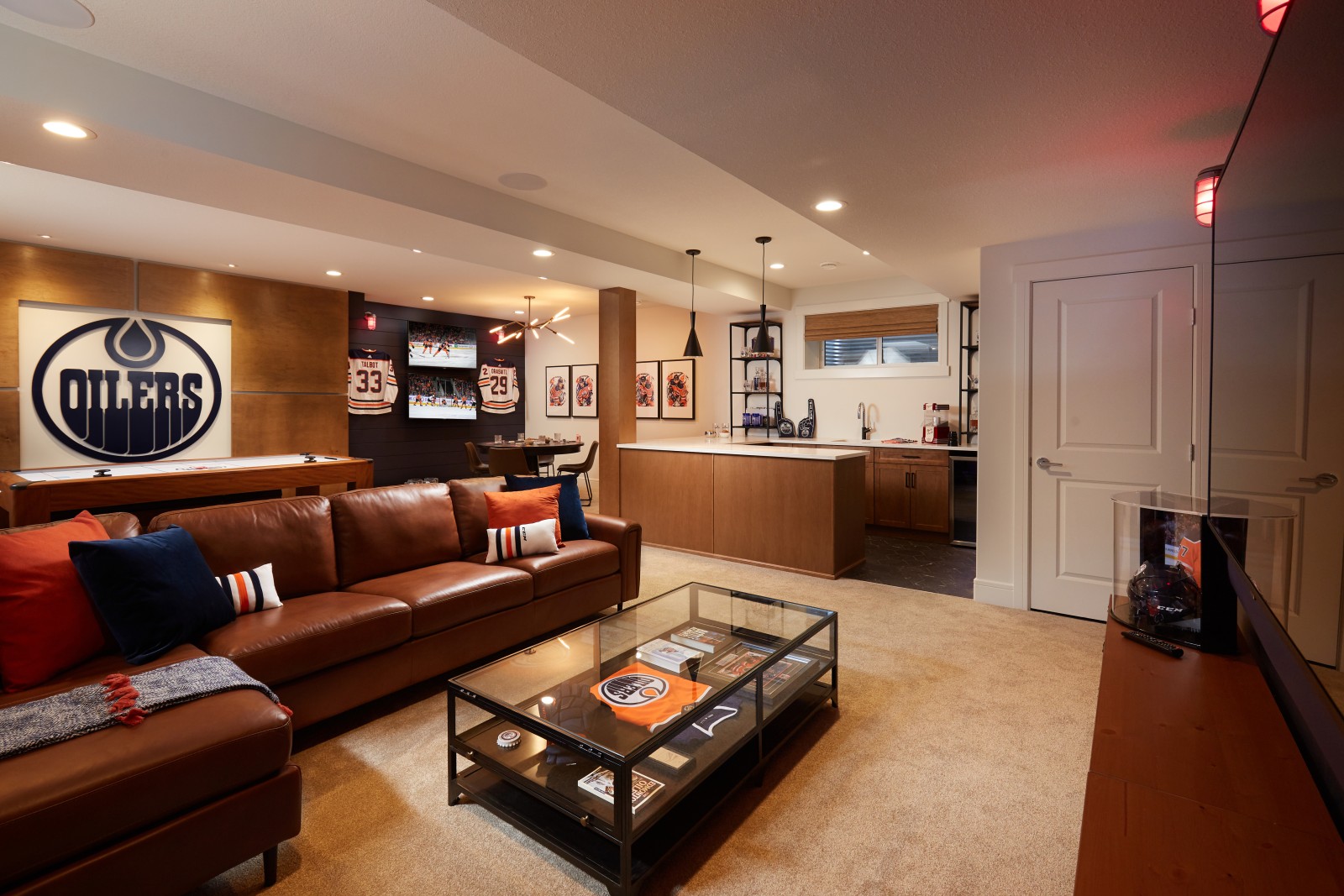 Exciting Fan Cave in the Archer showhome with warm wood bar, dark blue shiplap feature wall with two tv's and two mounted jerseys