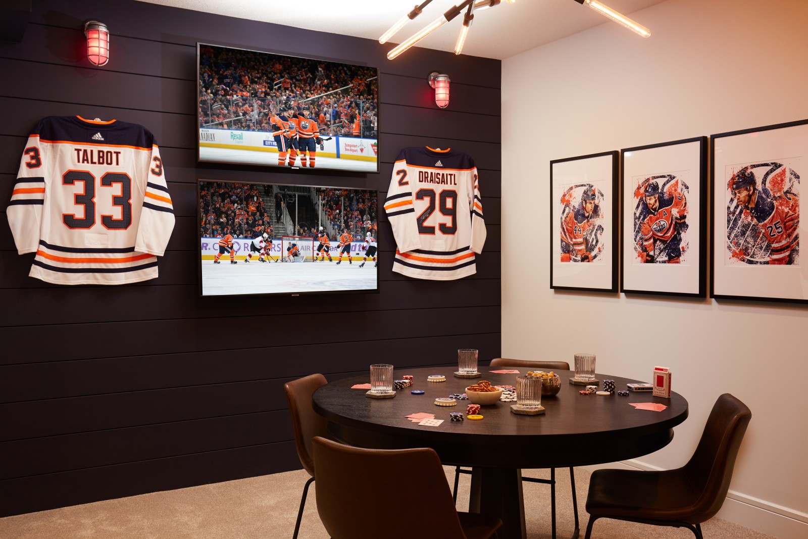 A games table set up in front of a dark blue shiplap feature wall with 2 tv's mounted and two jersey's