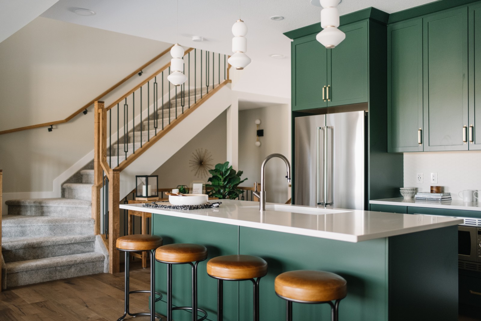 Bold green kitchen cabinets with warm stained railing leading to the second floor create an inviting atmosphere