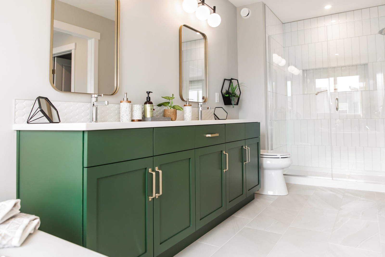 Bright ensuite in Bianca showhome with bold green dual vanity, gold mirrors, fully tiled shower with vertically stacked, white, subway tile