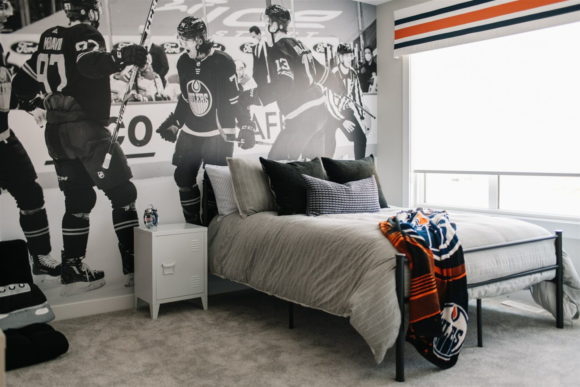 A fun Oilers bedroom with large mural of team behind the bed and oilers striped valance on window