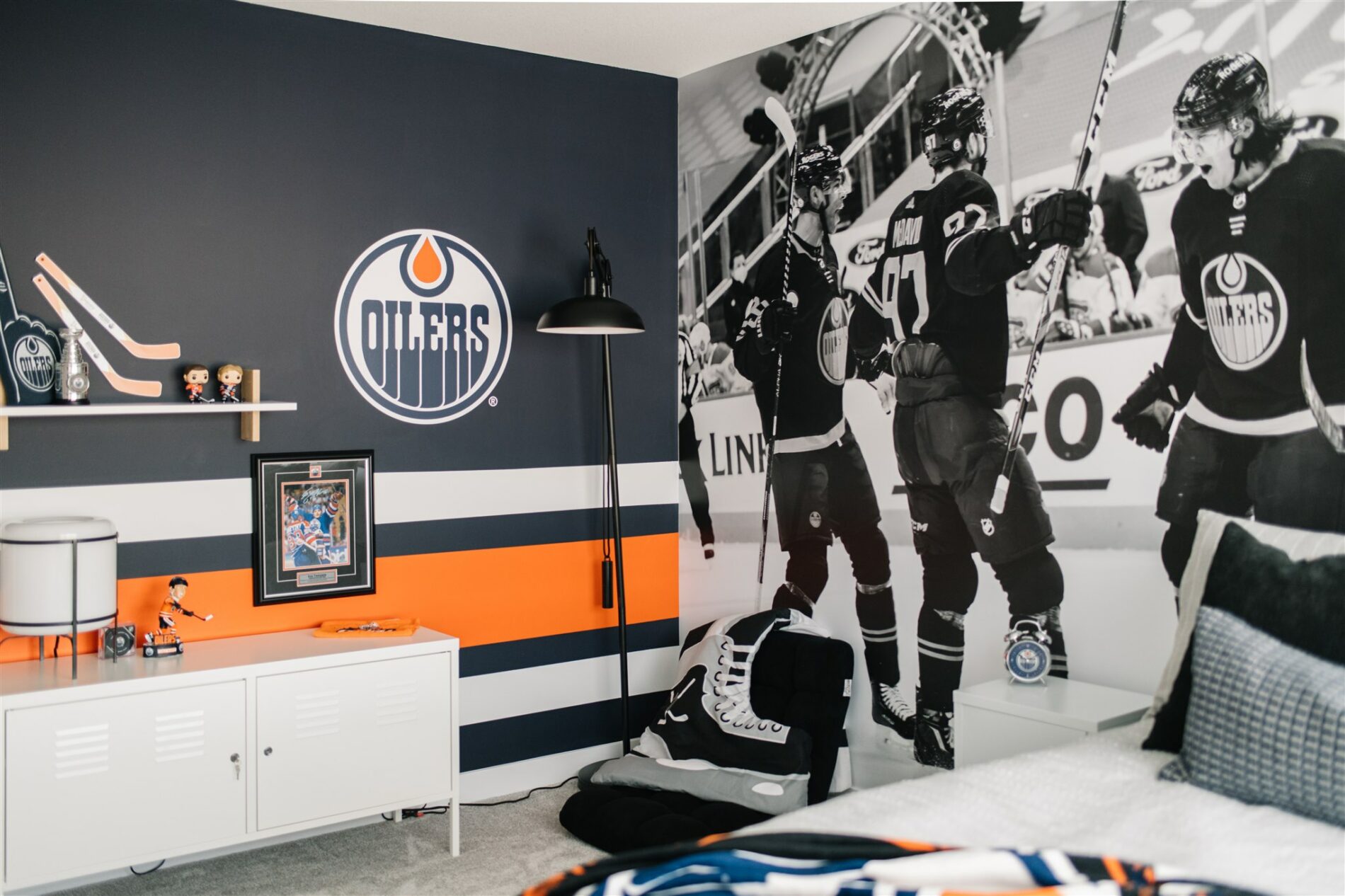 Fun Oilers bedroom with large mural of team celebrating, striped blue, orange and white feature wall with Oilers logo and hockey accesories