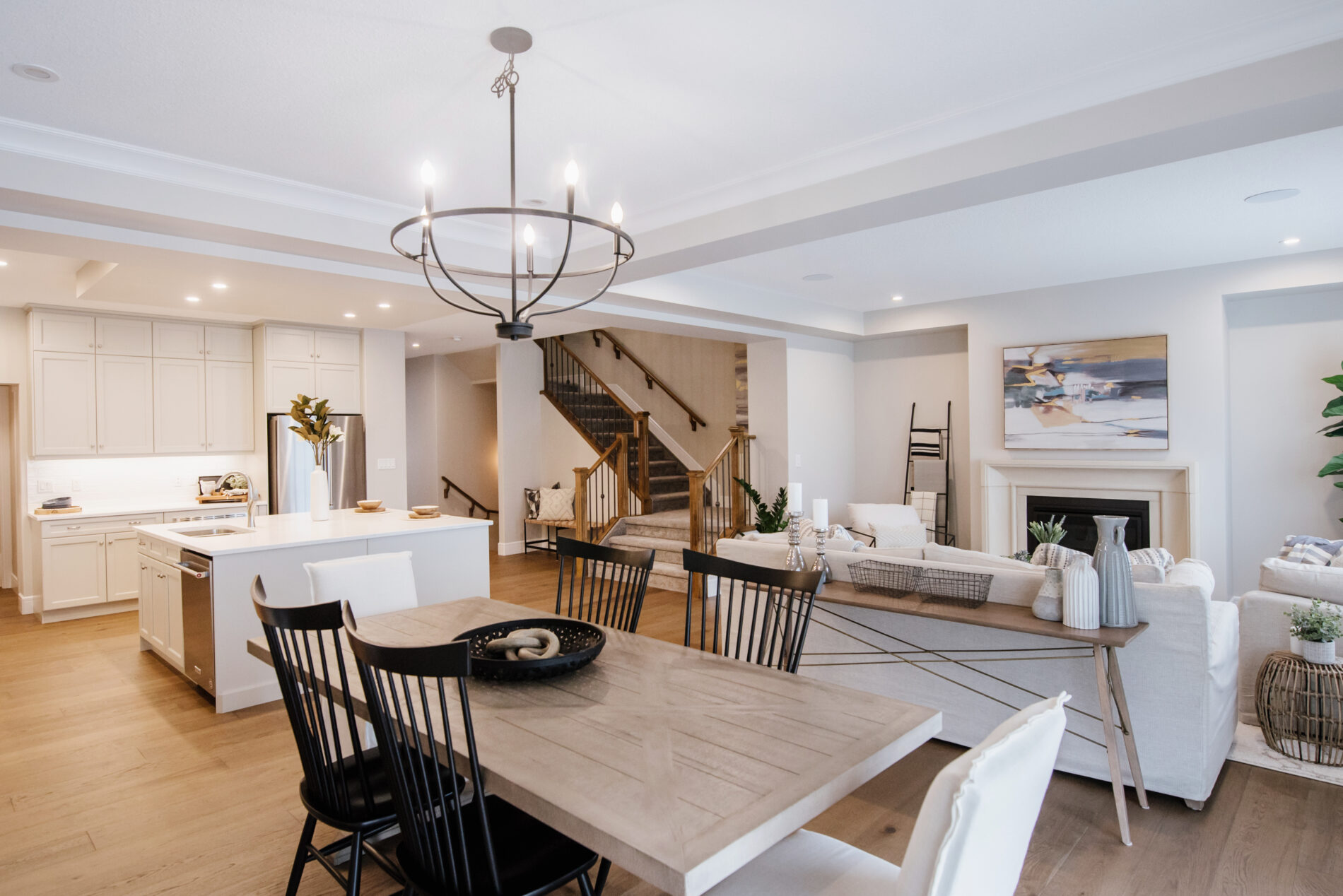 Photo of the open concept main floor of the Kalliope showhome in Ardrossan. Showing the dining room closest, the warm inviting living room with fireplace to the right and the light and bright kitchen to the left