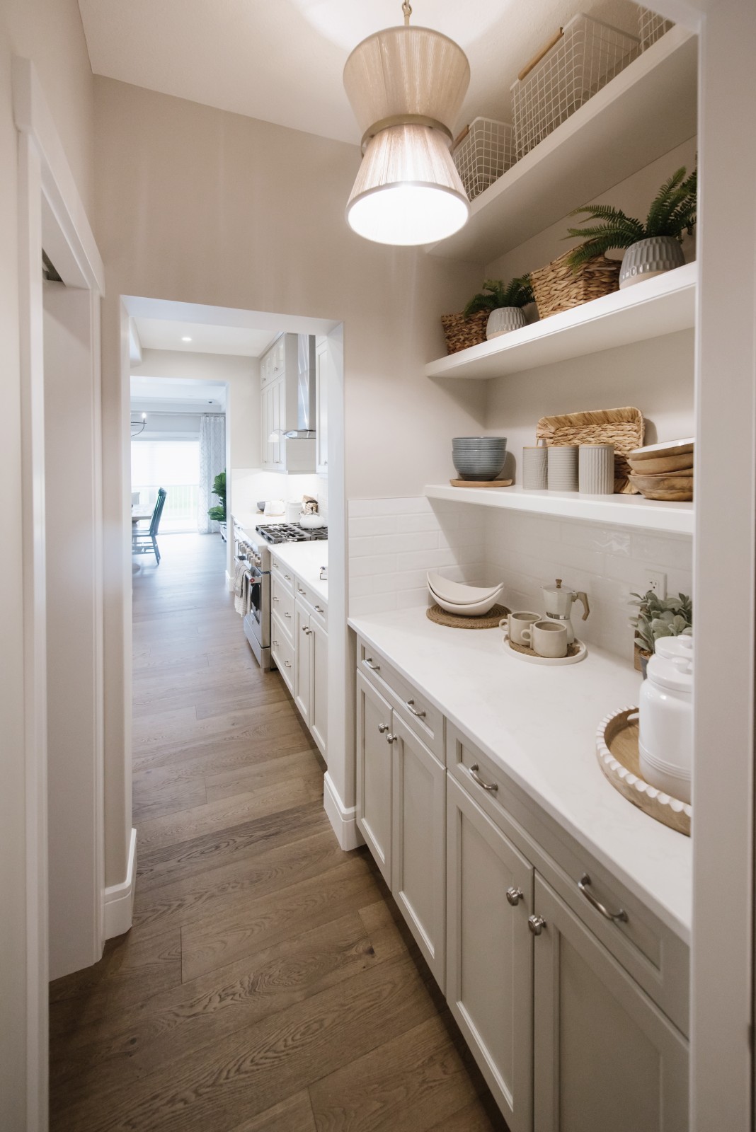 The walk through butlers pantry of the Kalliope showhome with light grey/beige cabinets, white countertops, two white floating shelves and light and natural toned accessories