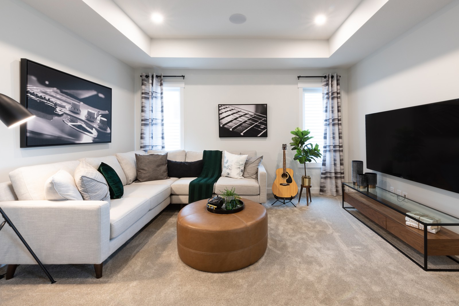 Cozy second floor bonus room with tray ceiling detail, inviting sectional couch, cognac upholstered ottoman, music inspired art work and guitar in the corner