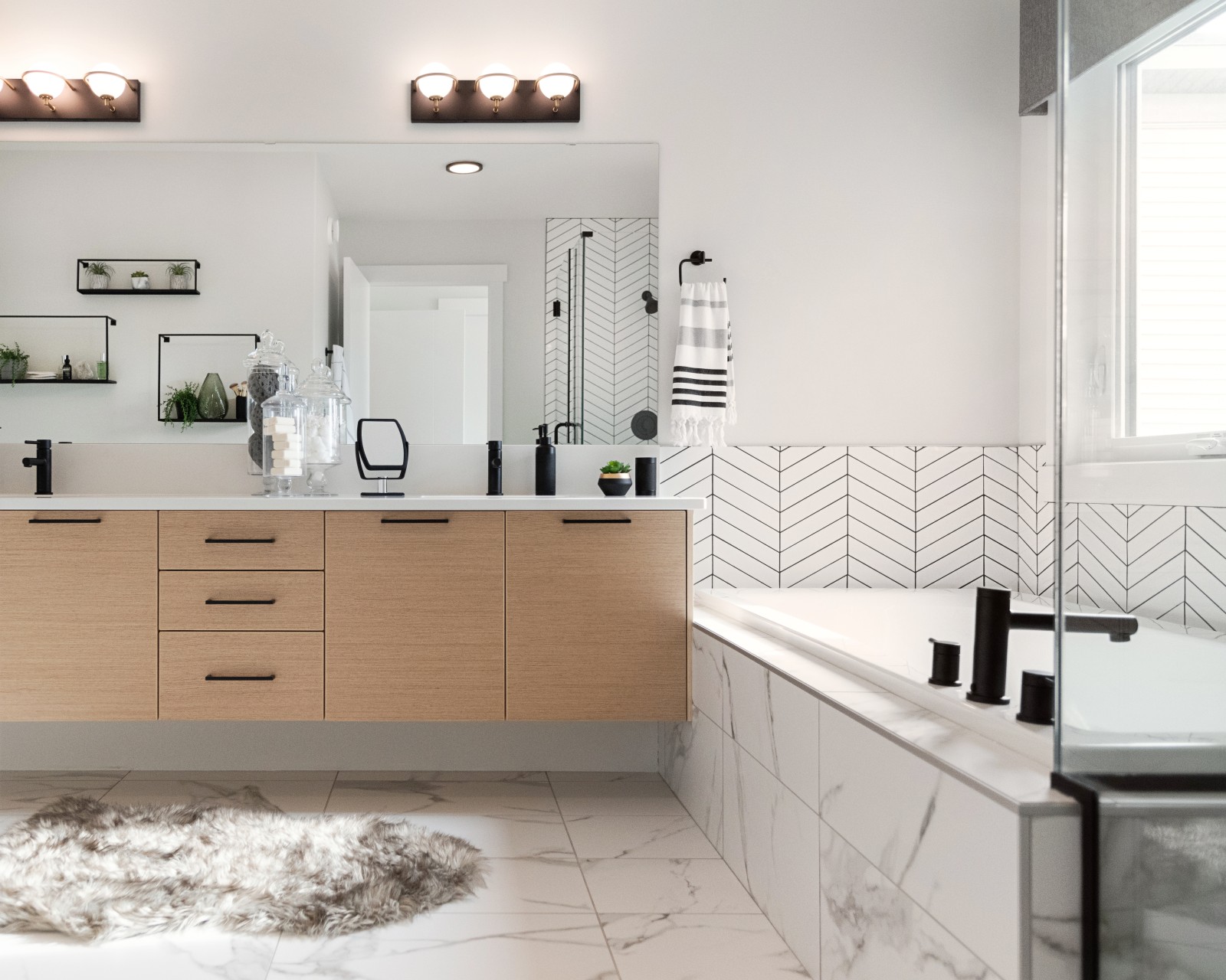 The master ensuite featuring natural wood, floating vanity with white countertops, black fixtures and soaking tub with modern chevron wall tile surround