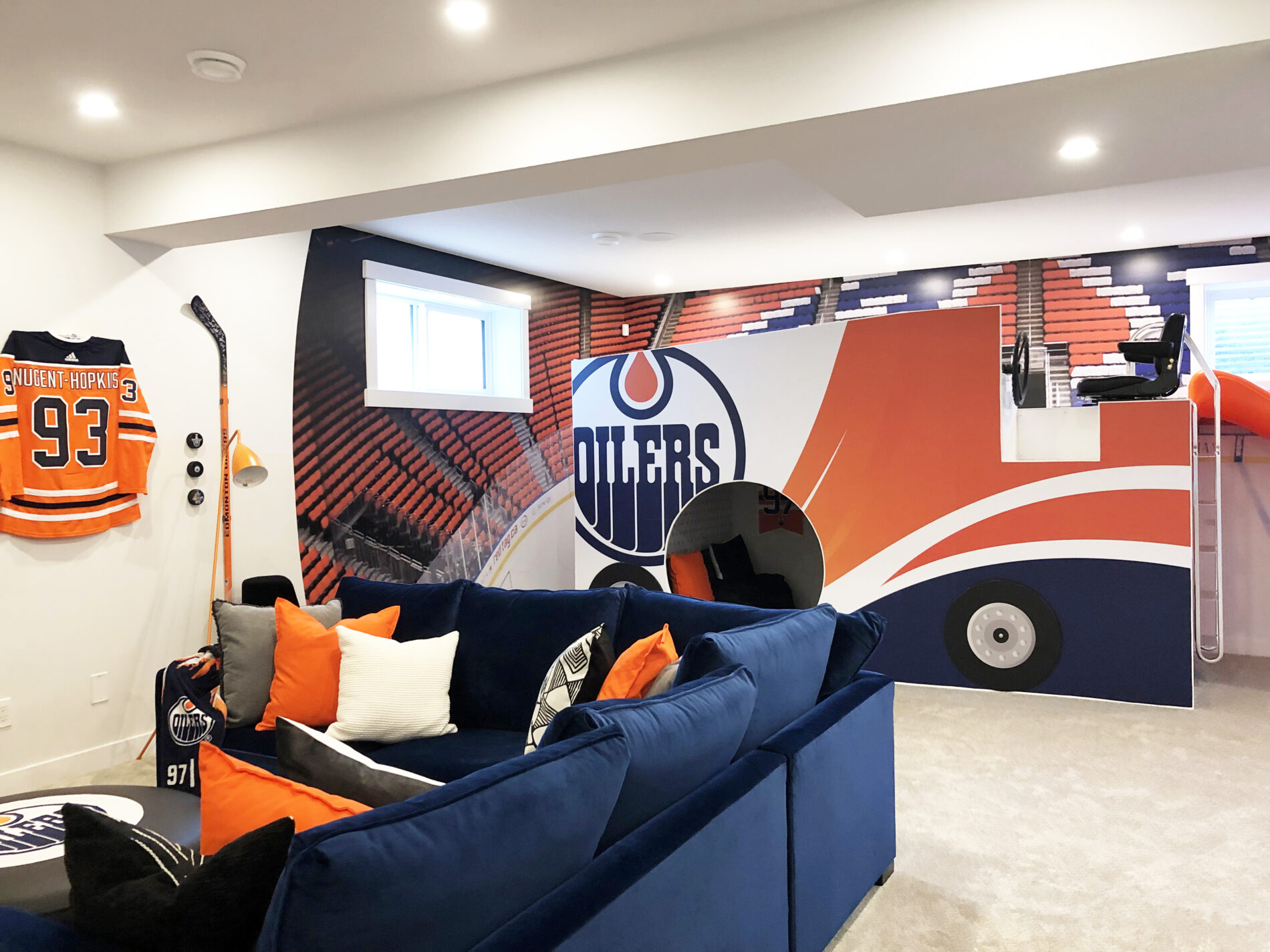 Zamboni play structure in basement Oilers Fan Cave in Dione showhome with wall mural of the stands of Rogers Place arena on the walls behind