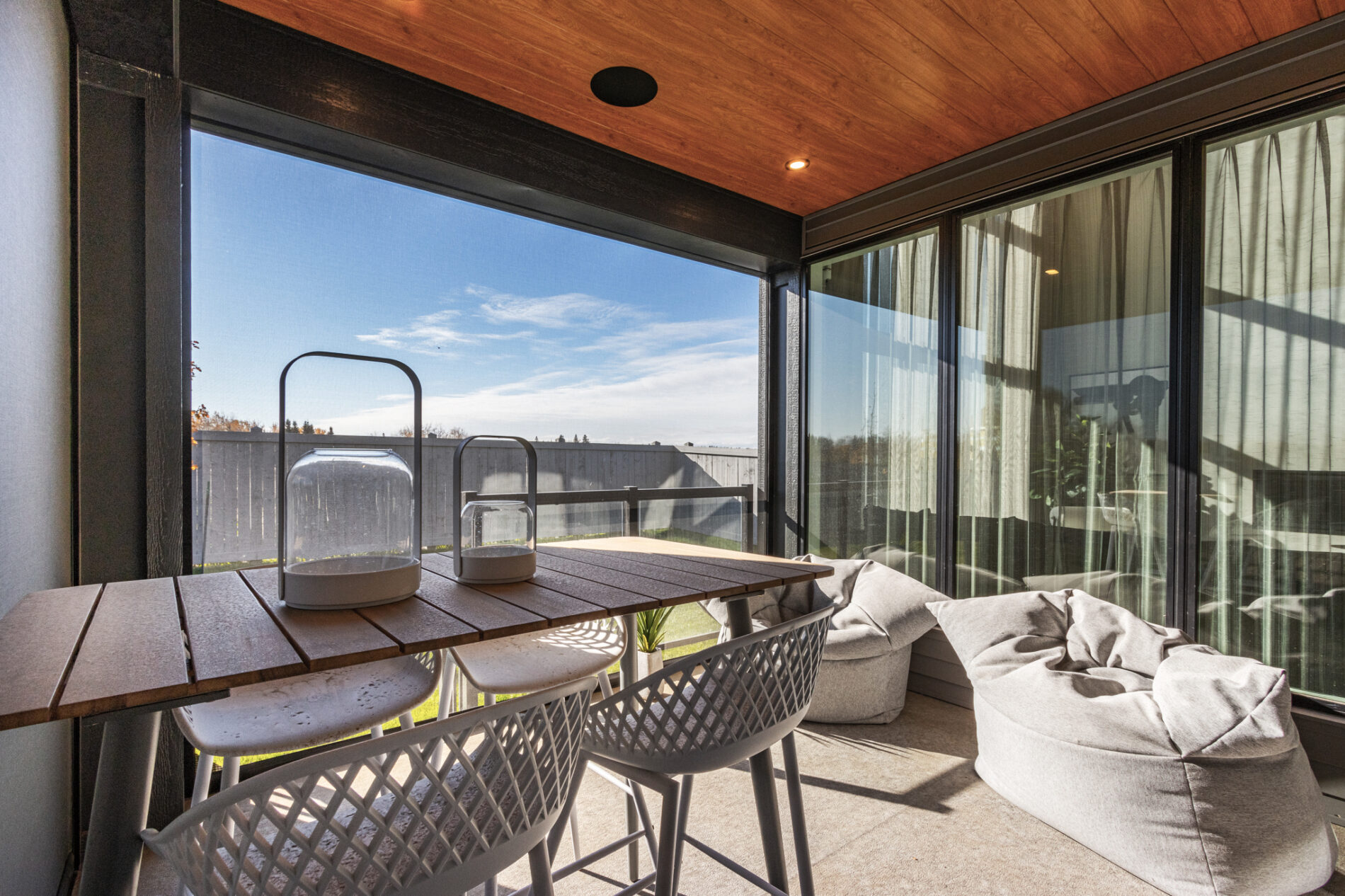 A bar table with four seats and two comfortable, modern, bean bag chairs are enclosed in the covered deck with warm wood ceiling detail