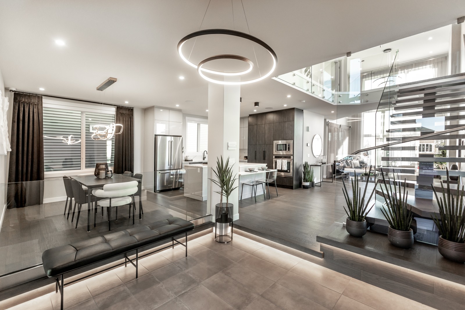 An overall photo of the open concept main floor of the Cyrus showhome showing the foyer, dining room, kitchen, custom staircase and open-to-above great room
