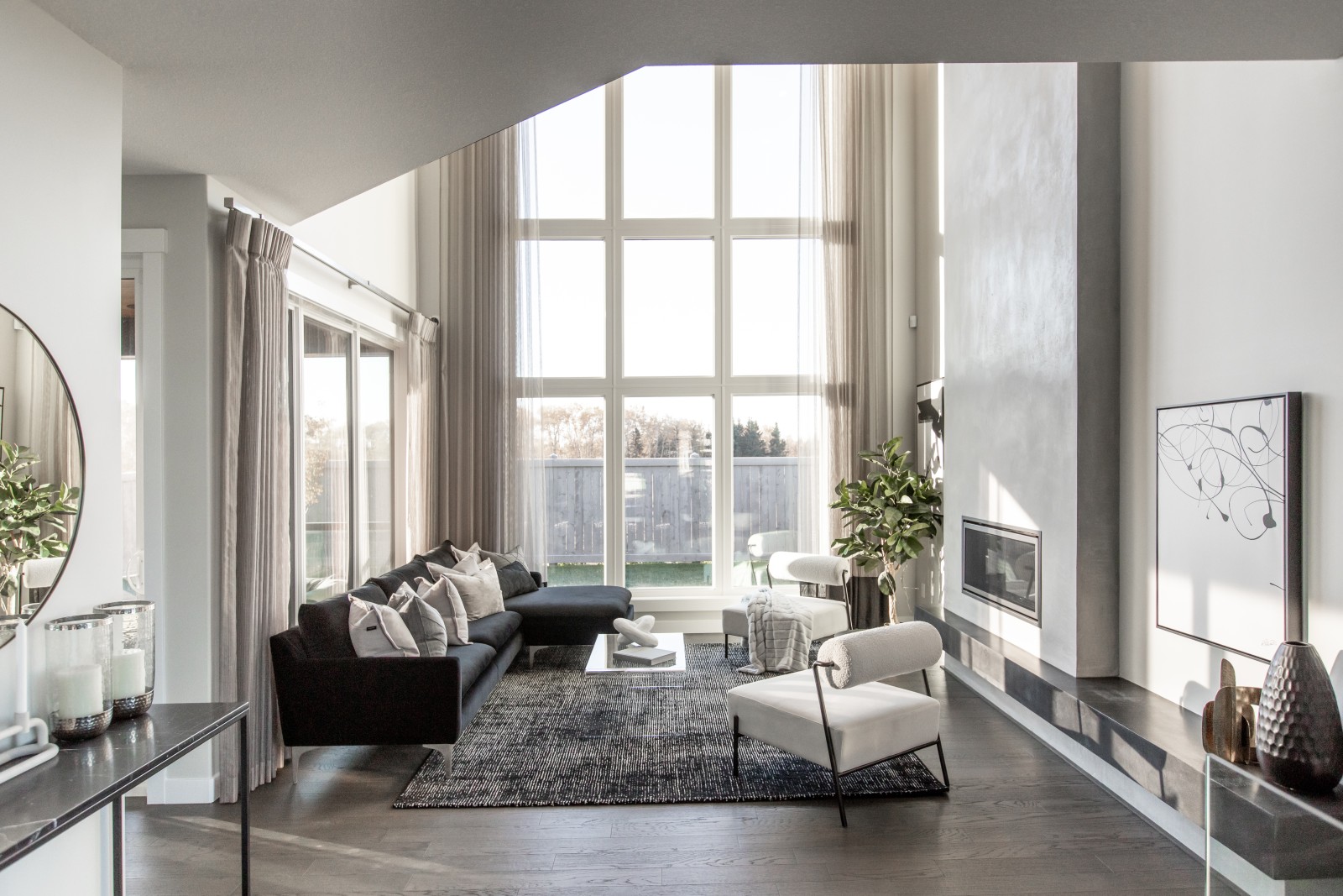 Natural light floods in through 2-storey windows in the great room highlighting the modern 2-storey plaster fireplace and sleek furniture