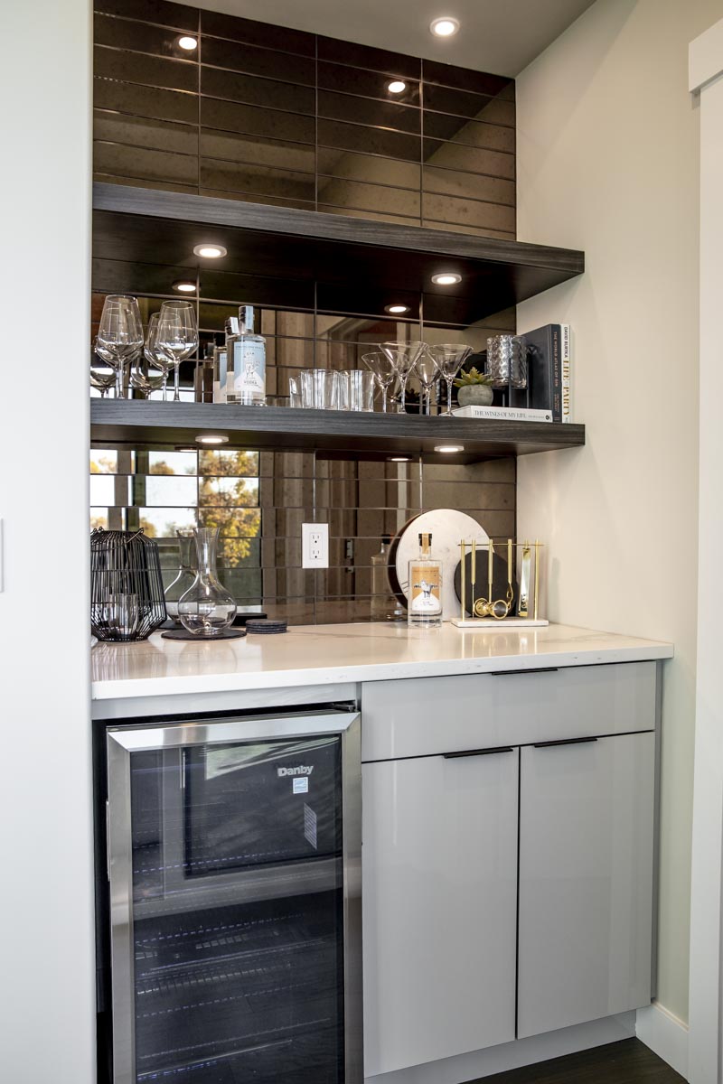 Dry bar with sleek grey cabinets, floating shelves with mirrored tile behind to the ceiling