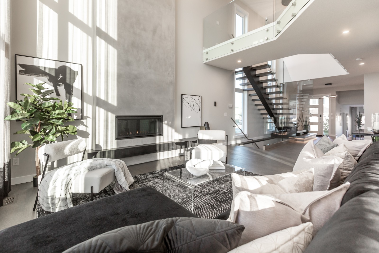 Open to above great room of the Cyrus showhome with two-storey, modern plaster fireplace, open riser staircase with glass railing
