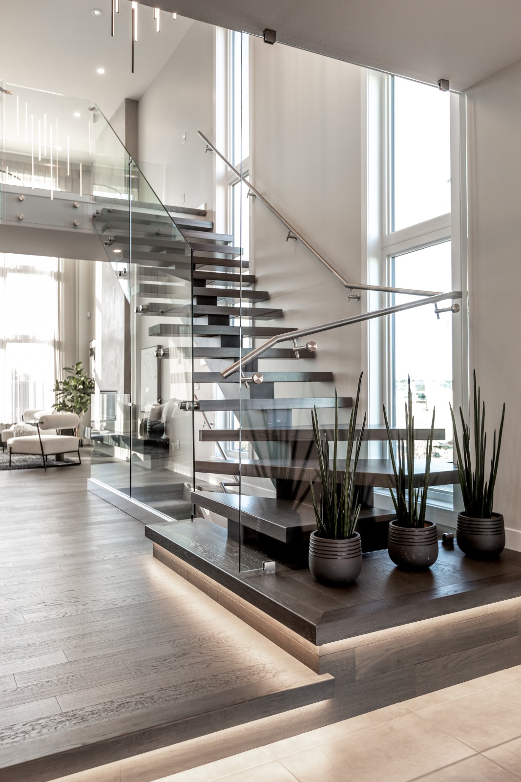 The modern staircase in the Cyrus showhome with open wood treads, steel spine, and glass rail and sleek steel handrail leads up to the second floor