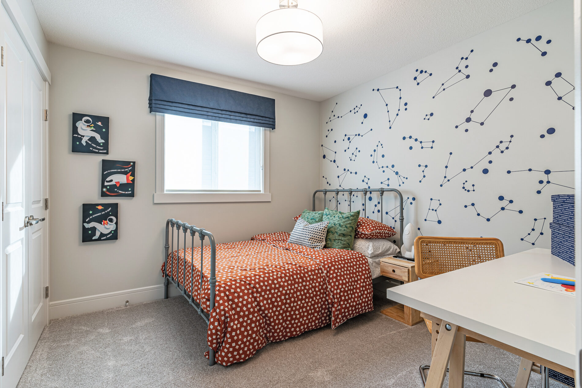 A secondary bedroom with blue constellation decals behind the wrought iron bed with orange bedding