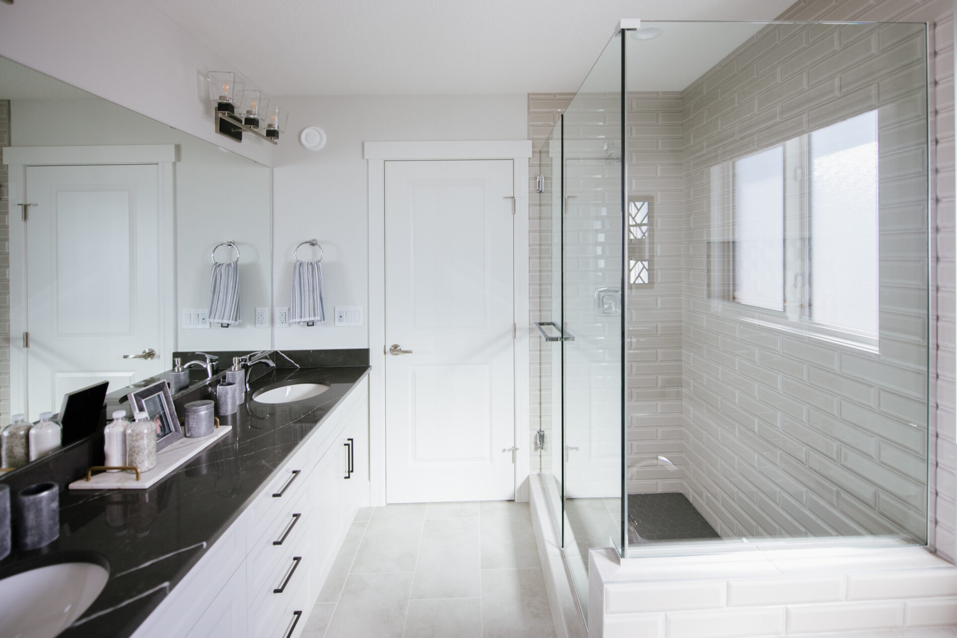 A bright ensuite with white cabinets, dark countertops, fully tiled shower and soaker tub