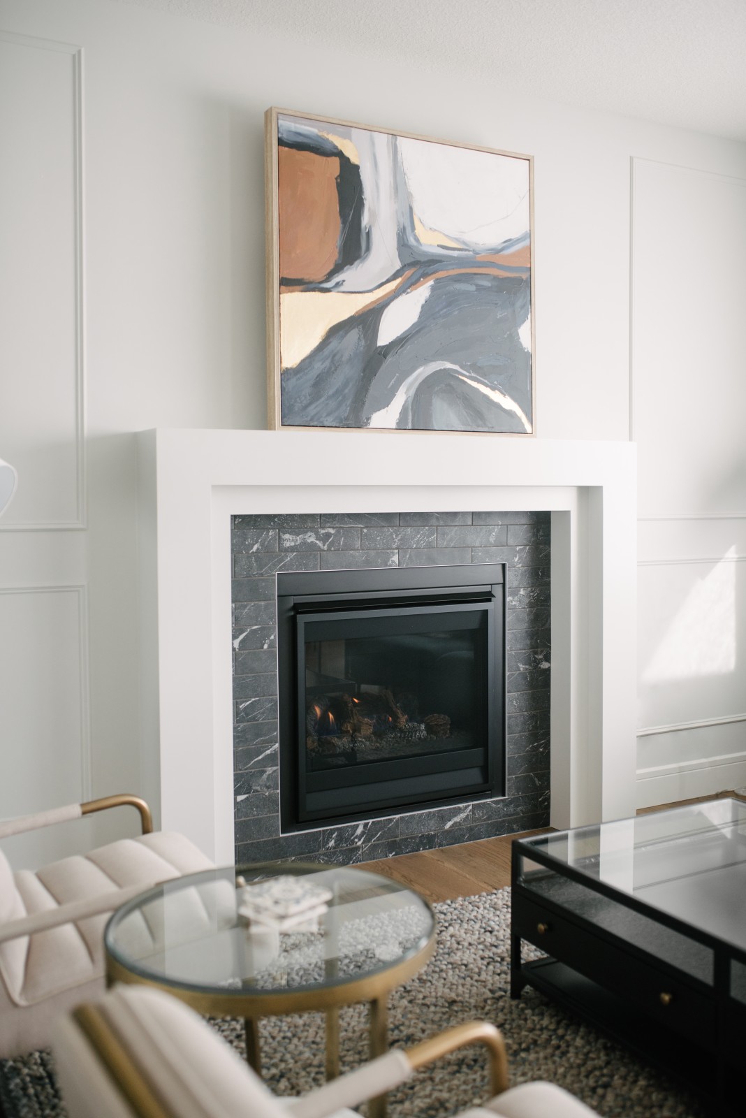 A classic fireplace with black tile, and white mantle on a wall with simple moulding detail on the wall. A large framed piece of abstract art sits on the mantle