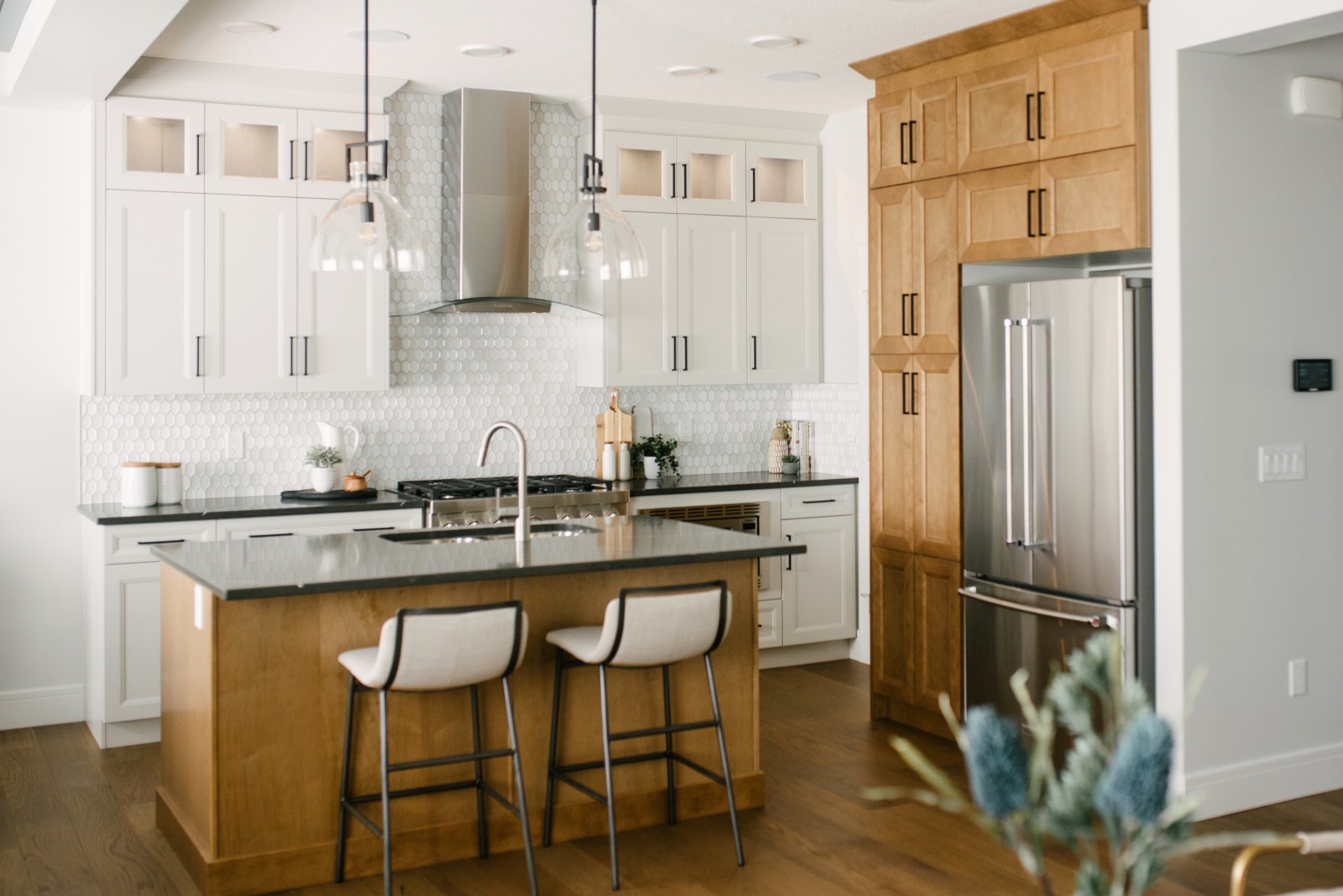 A two-toned white and warm wood kitchen with dark countertops and complimenting hardwood floors