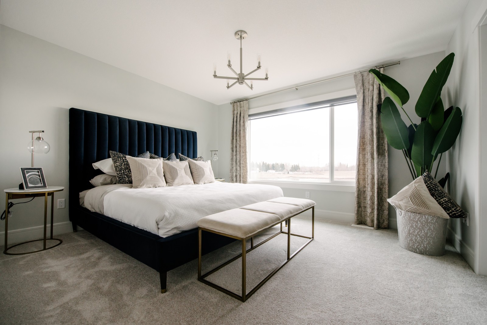 Spacious master bedroom with large window spanning the back of the room with a large dark blue upholstered bed