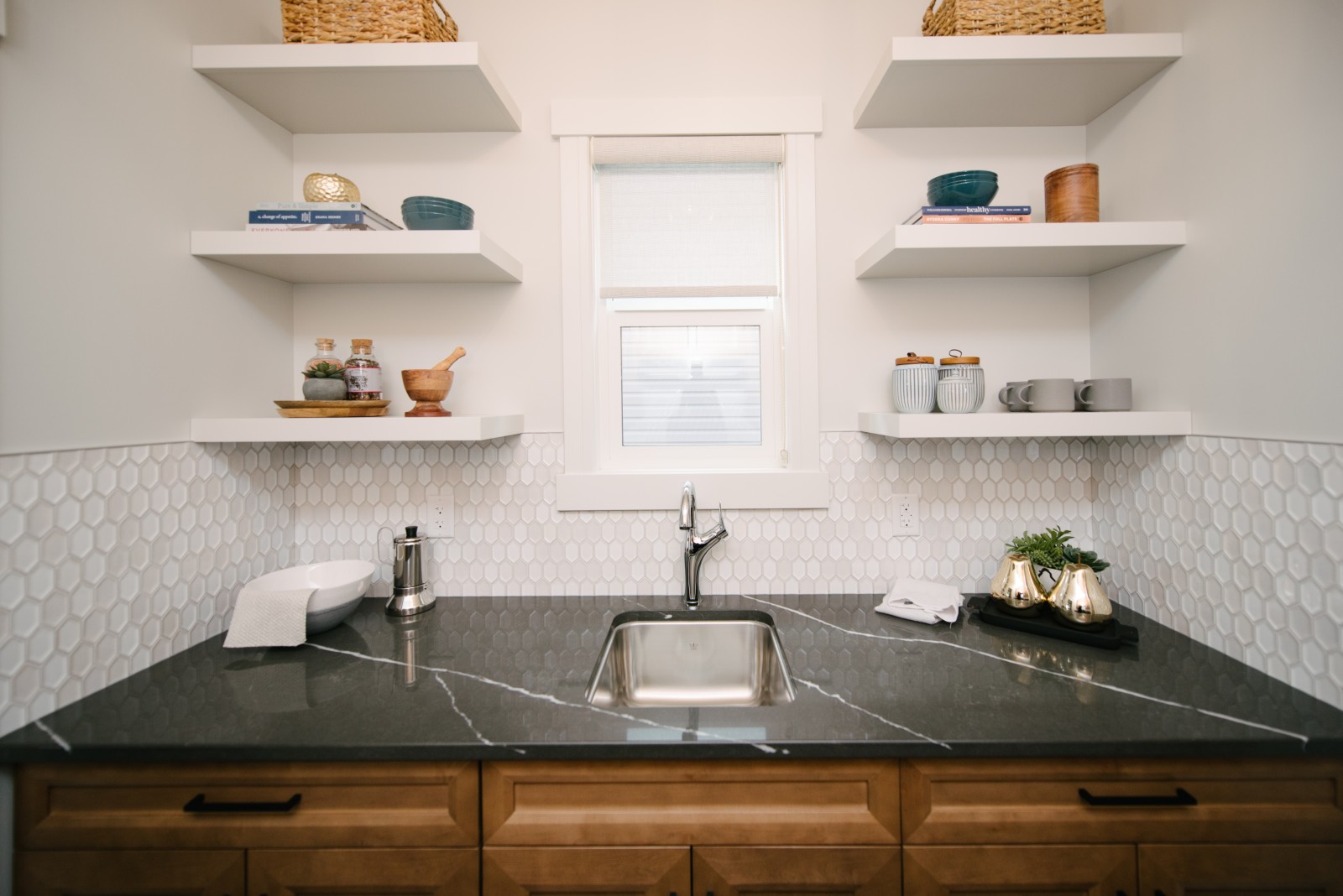 The window of the Spice Kitchen flanked by white floating shelves above dark countertops and warm wood cabinets