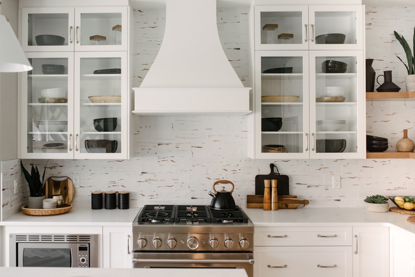 Range wall of the Cyrus showhome that features a white, wood hood fan flanked by upper cabinets with glass fronts staged with dishes