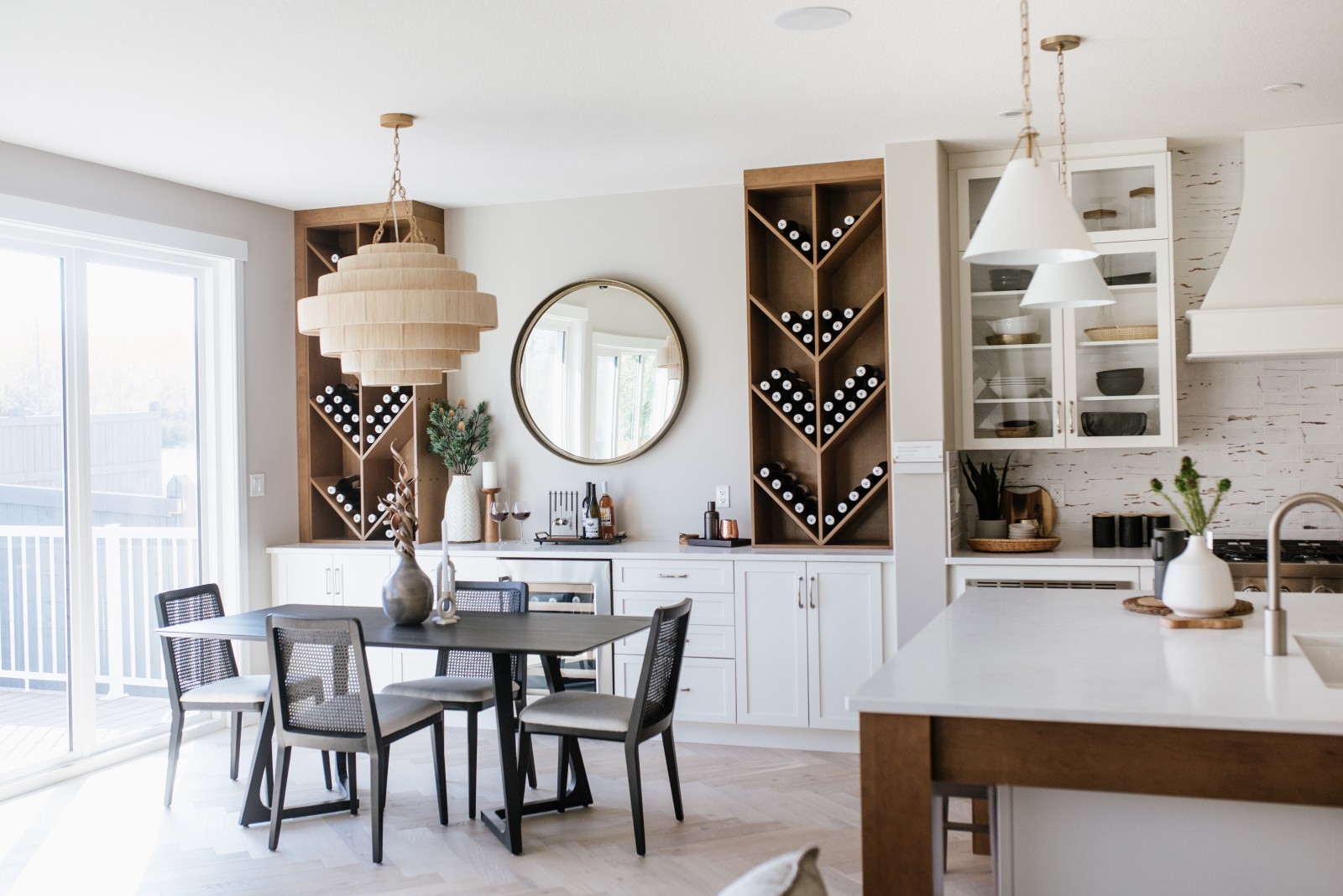 A dining nook with white side buffet cabinets and custom, wood, geometric wine racks flanking a round mirror