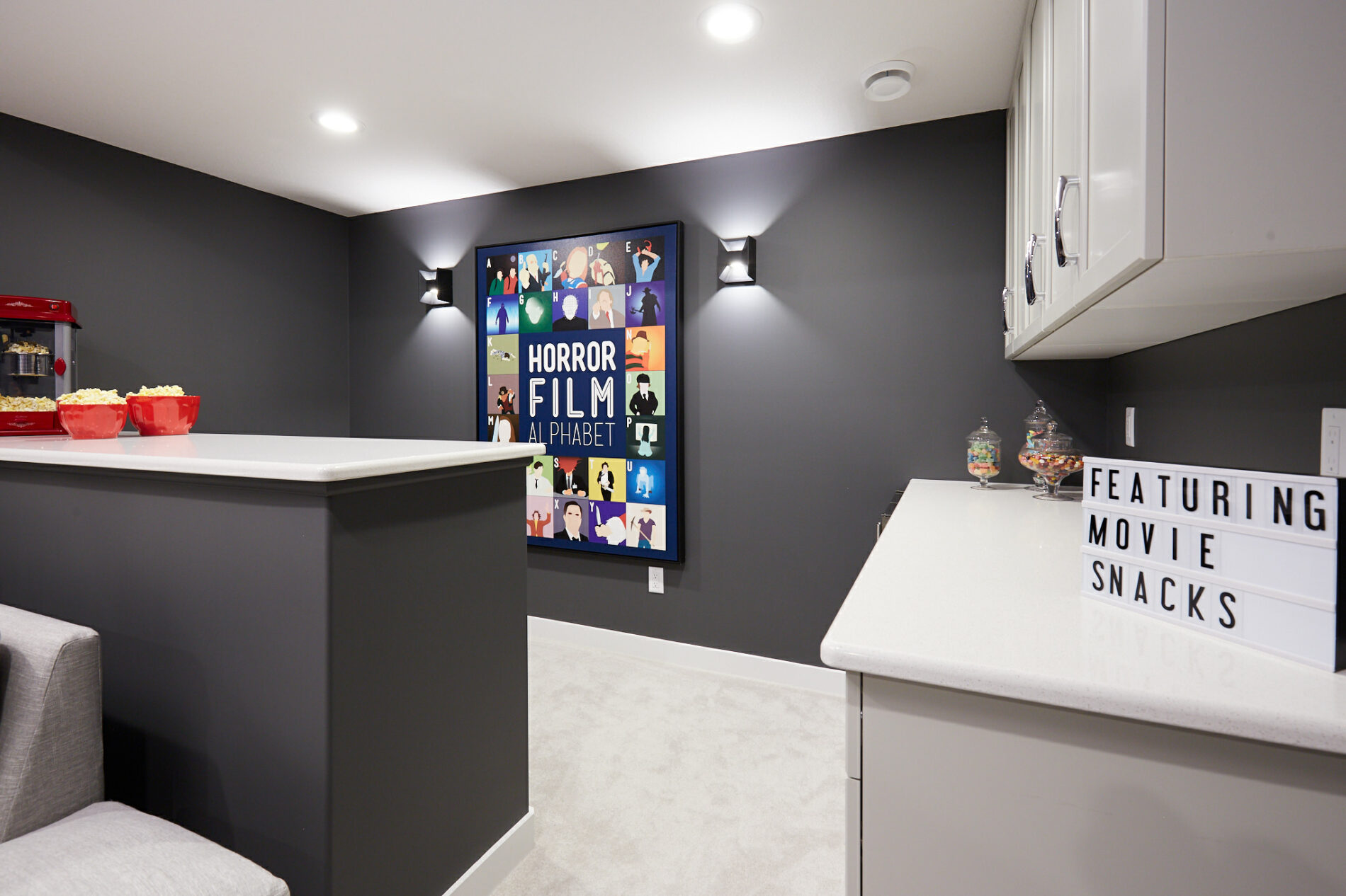 Theatre room in basement with dark grey wall, light cabinetry and a large colourful movie themed piece of art