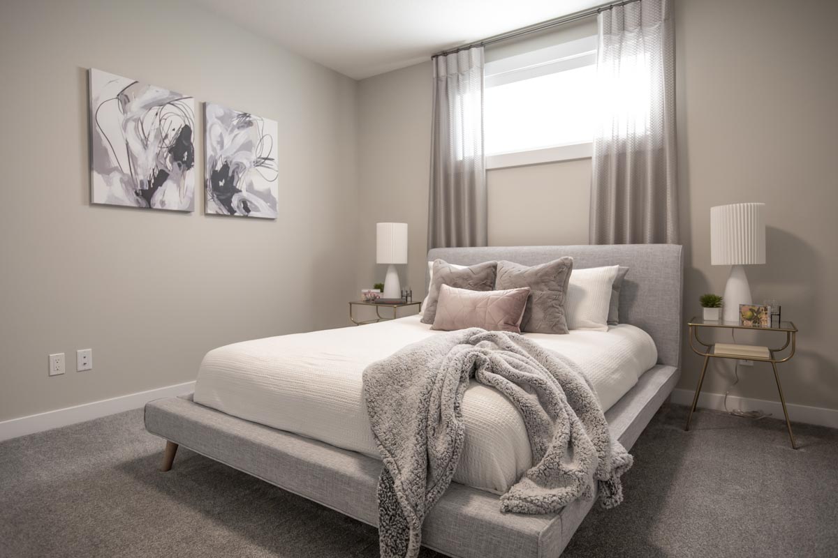 Bedroom in basement with light coloured bed placed under the bright window