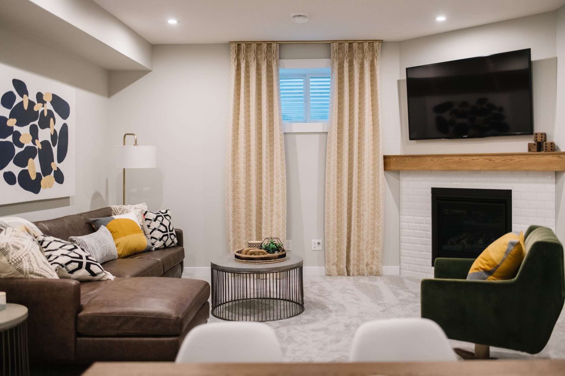 Family room in basement with corner fireplace, grey sectional across and rich green accent chair