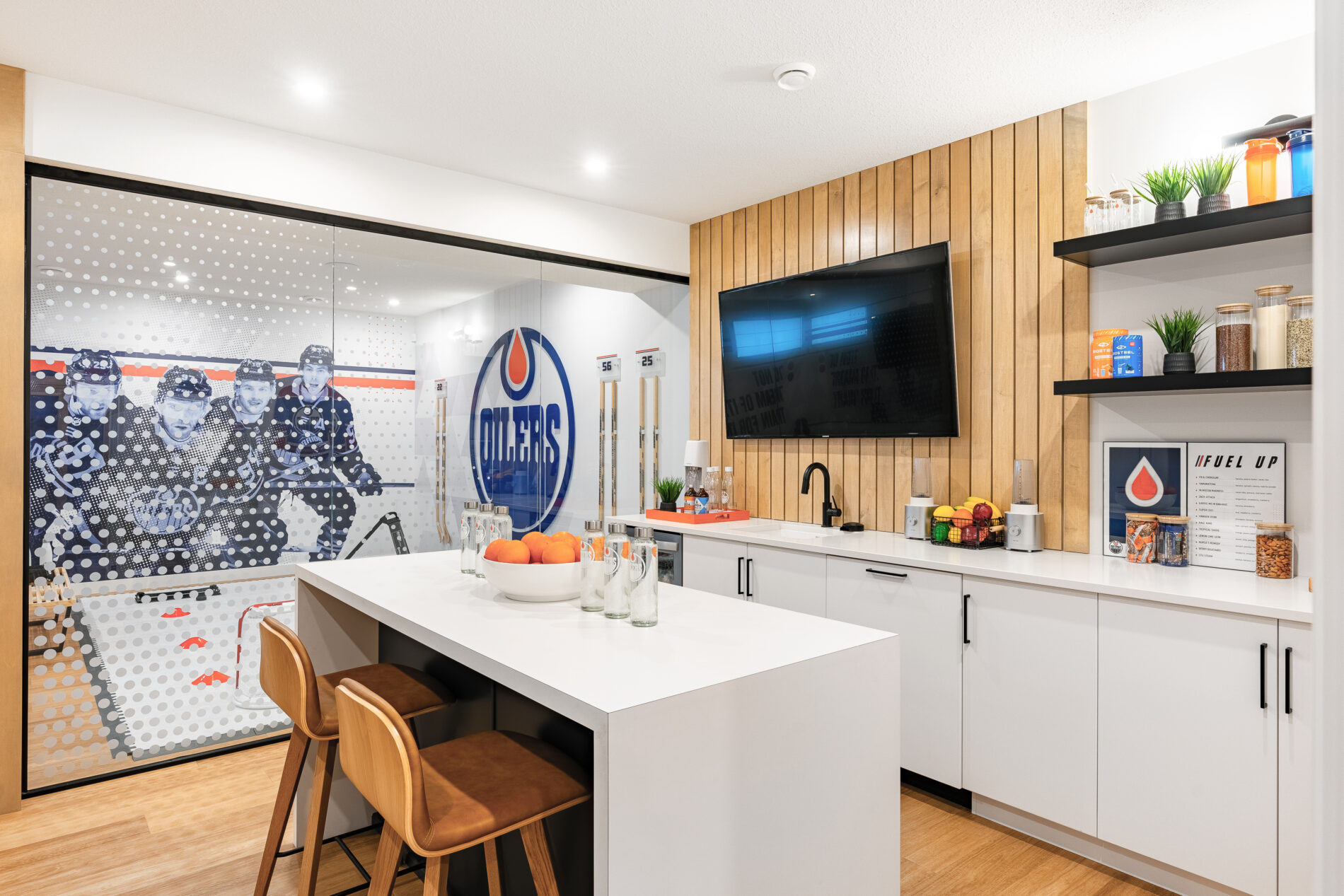 Nordic inspired smoothie bar with white walls, cabinets and countertops with wood slat wall behind tv in Oilers Fan Cave Basement