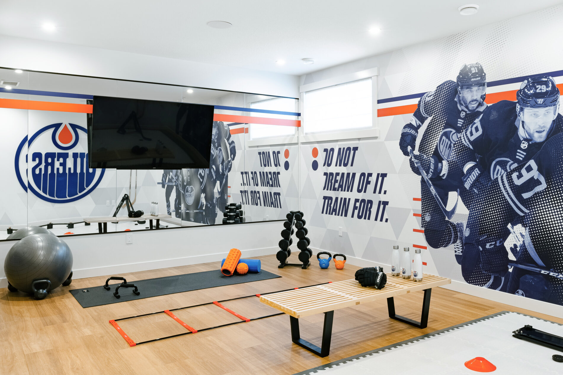 Training gym with muraled Edmonton Oilers walls, mirrored wall, light flooring and training equipment on floor in Oilers Fan Cave